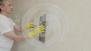 Plasterer man holding putty knife is spackling patching a hole in white wall.