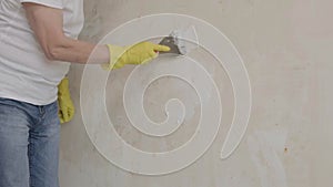 Plasterer man holding putty knife is spackling patching a hole in white wall.