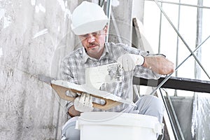 Plasterer man at work, take the mortar from the bucket to plastering the wall of interior construction site wear helmet and