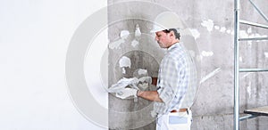 Plasterer man at work with trowel plastering the wall of interior construction site wear helmet and protective gloves, scaffolding