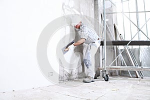 Plasterer man at work with trowel plastering the wall of interior construction site wear helmet and protective gloves, scaffolding
