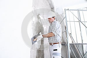 Plasterer man at work with trowel plastering the wall of interior construction site wear helmet and protective gloves, scaffolding