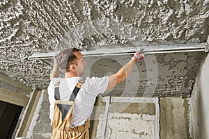 Plasterer smoothing plaster mortar on ceiling with screeder