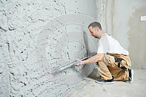 Plasterer using screeder smoothing putty plaster mortar on wall photo