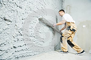 Plasterer using screeder smoothing putty plaster mortar on wall photo