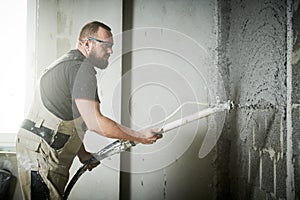 Plasterer using screeder spraying putty plaster mortar on wall