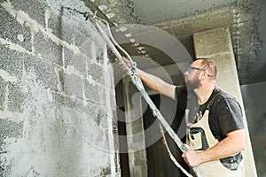 Plasterer using screeder spraying putty plaster mortar on wall