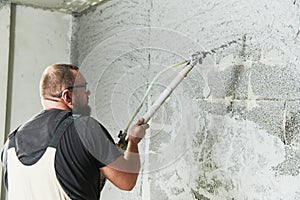 Plasterer using screeder spraying putty plaster mortar on wall