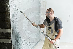 Plasterer using screeder spraying putty plaster mortar on wall