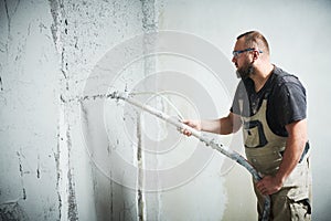 Plasterer using screeder spraying putty plaster mortar on wall