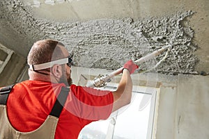 Plasterer using sprayer machine putting plaster mortar on ceiling