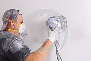 Plasterer wearing dust mask polishes a wall with sanding machine