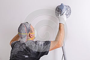 Plasterer wearing dust mask polishes a wall with sanding machine