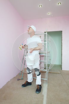 Plasterer in white clothes and kneepads looking at