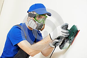 Plasterer worker with sander at wall filling