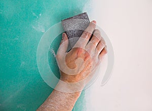 Plastering man hand sanding the plaste in drywall seam