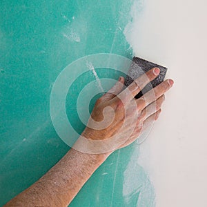 Plastering man hand sanding the plaste in drywall seam photo