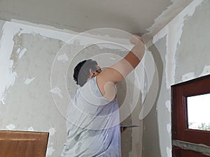 Plasterwork and wall painting preparation. Asian male applying plaster or filling drywall patch