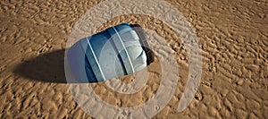 Plastic blue drum lying in rippled sand of beach.