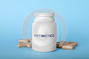 Plastic bottle with antibiotic pills on light blue background
