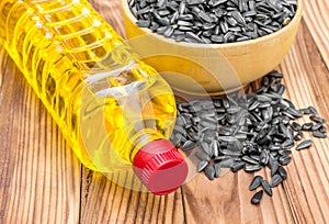 Plastic bottle of cooking oil with bowl of sunflower seeds on wooden background