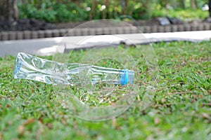 A plastic bottle of drinking water littering on  pathway with green field background,for saving an environmental concept