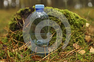 Plastic bottle of fresh water on ground in forest