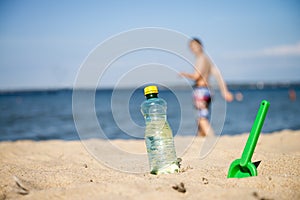 Plastic Bottle of fresh water is on the sand by the sea. Drinking water in bottle on sand on beach. Bottle of fresh