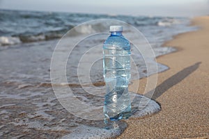 Plastic bottle of fresh water on wet sand near sea