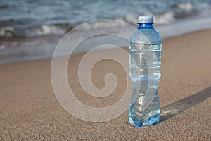 Plastic bottle of fresh water on wet sand near sea. Space for text