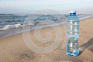 Plastic bottle of fresh water on wet sand near sea. Space for text