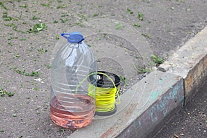 Plastic bottle with fuel and a string on the sidewalk in the city. Materials for mowing the lawn with a hand mower