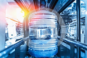 Plastic bottle or gallon of purified drinking water inside automated conveyor production line. Water factory, blue toned