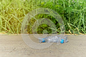 Plastic bottle garbage waste is thrown on the ground with blur green nature background.