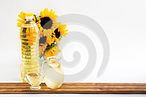 Plastic bottle and glass jars with sunflower oil and bouquet on wood