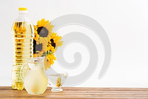 Plastic bottle and glass jars with sunflower oil and bouquet on wooden table