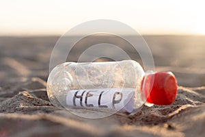 A plastic bottle with the message help inside lies on the sand of a beach close-up. concept save the planet from plastic