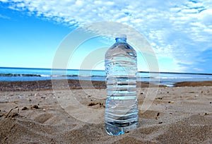 Plastic bottle with mineral water on beach by sea. PET bottle on the sand.