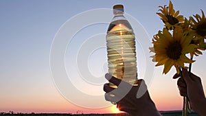 Plastic bottle of oil and sunflower flowers on a background of pink sunset.