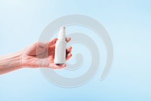 Plastic bottle with sanitizer in spray in female hand over blue background