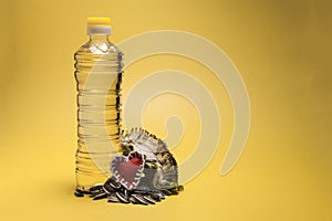 Plastic bottle with vegetable oil, red heart and sunflower seeds on a yellow background