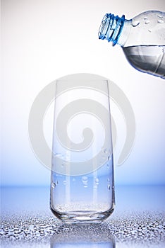 Plastic bottle with water over empty drinking glass