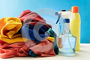Plastic bottles of cleaning products set with pile clothes on white table background