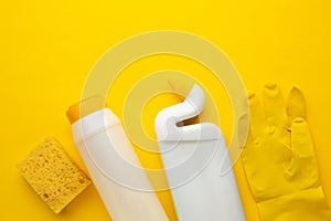 Plastic bottles of cleaning products, sponge and glove on yellow background with space for inscription