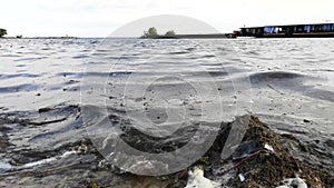 Plastic bottles and glasses on the sandy beach. Dirty water in which zllichny garbage floats. White foam on the shore