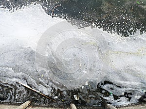 Plastic bottles and glasses on the sandy beach. Dirty water in which zllichny garbage floats. White foam on the shore