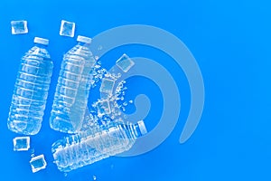 Plastic bottles with pure water and ice on blue background top view space for text