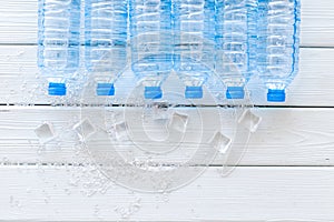 Plastic bottles with pure water and ice on white wooden background top view space for text