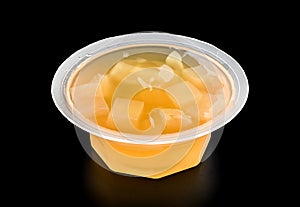 Plastic bowl with orange  jelly and pieces of fruit close-up isolated on black background