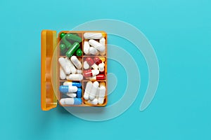 Plastic box close-up with different pills on blue background, top view. Empty place for text, copy space. Dietary supplements and